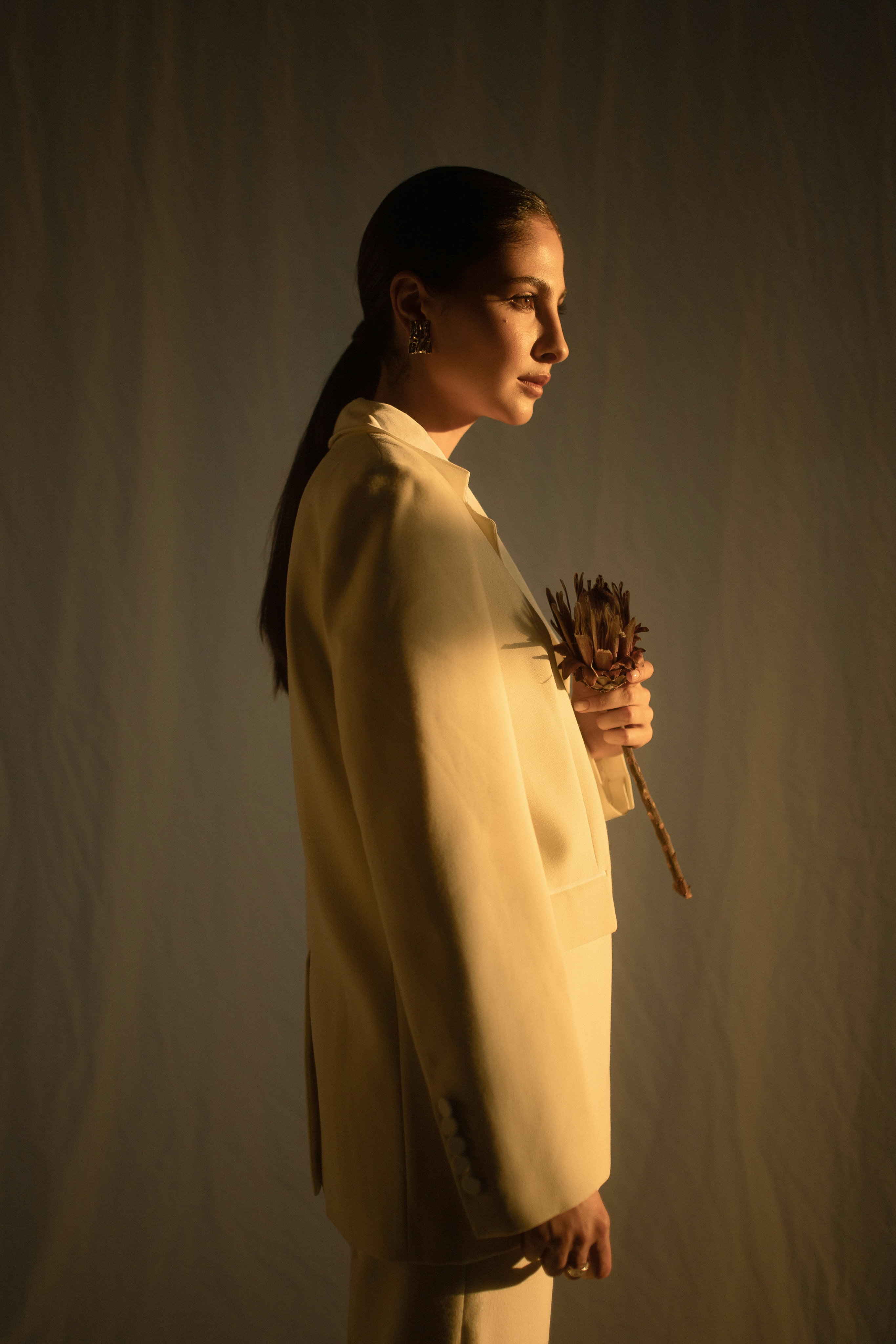 Woman in a suit, holding a flower, bathed in warm light